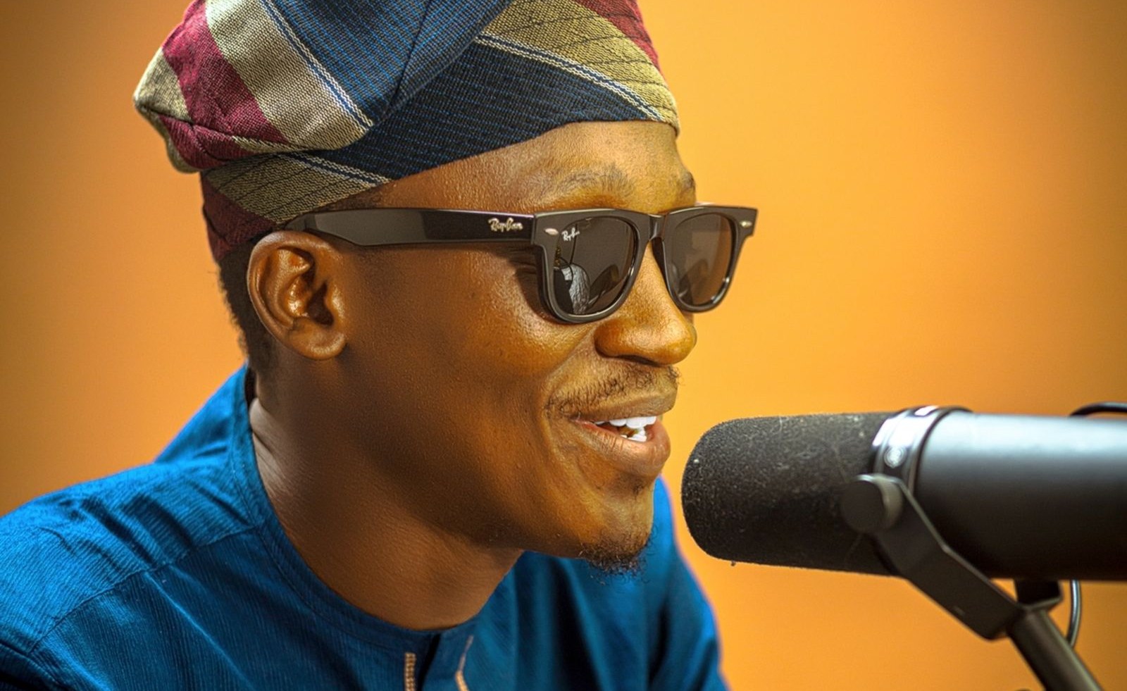 A man in traditional attire speaking into a broadcast microphone